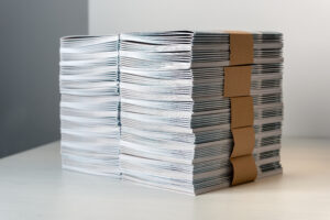 Bundles of newly printed catalogues fastened with brown paper arranged neatly in a stack on a white table